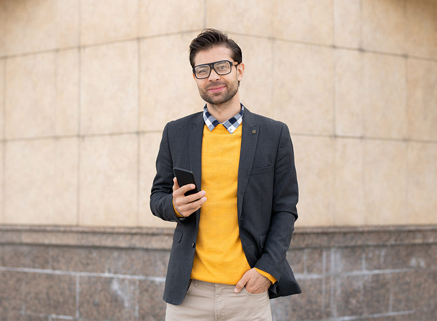 Smiling stylish young man wearing yellow sweater using cell phone depicting browsing professional resume packages